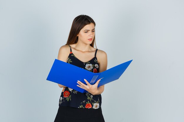 Portrait of young lady looking over folder in blouse and looking confused front view