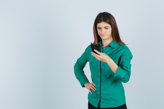 Portrait of young lady looking at mobile phone in green shirt and looking displeased front view