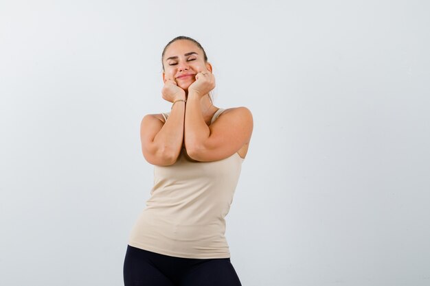 Portrait of young lady pillowing face on her hands in tank top and looking peaceful front view