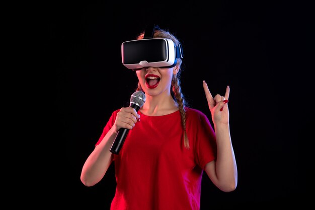 Portrait of young lady playing vr and singing on dark wall