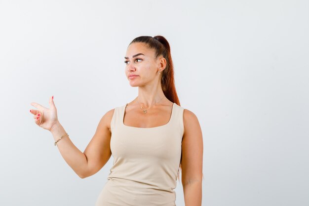 Portrait of young lady pointing aside in tank top and looking confident front view