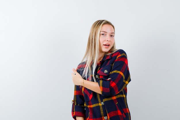 Portrait of young lady pointing back in checked shirt and looking positive front view