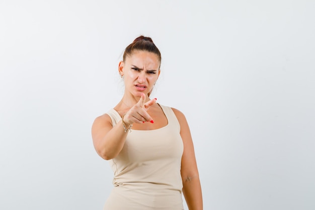 Portrait of young lady pointing at camera in tank top and looking angry front view