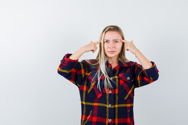 チェックのシャツで頭を指して、真剣な正面を見て若い女性の肖像画