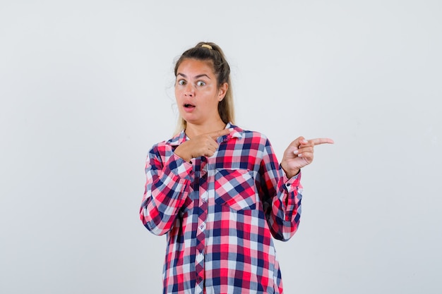 Portrait of young lady pointing to the right side in checked shirt and looking scared front view