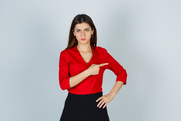 Portrait of young lady pointing to the right side in red blouse