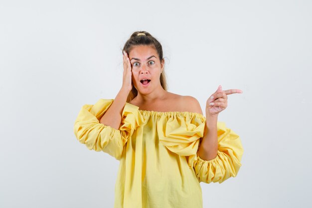 Portrait of young lady pointing to the right side in yellow dress and looking amazed front view