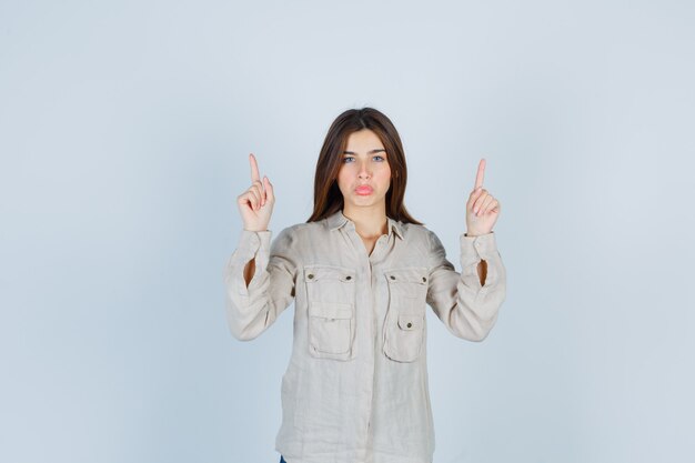 Portrait of young lady pointing up in casual, jeans and looking confident front view