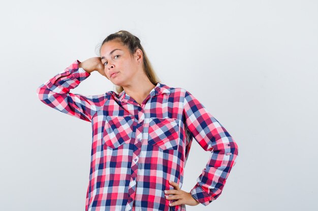 Portrait of young lady posing with hand on head in checked shirt and looking alluring front view