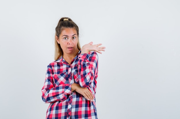 Portrait of young lady pretending to hold something in checked shirt and looking confident front view