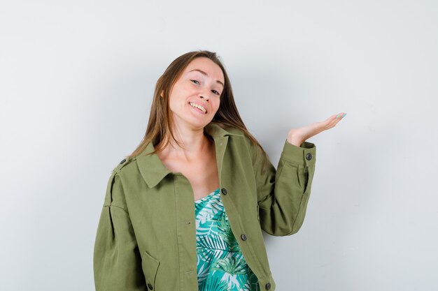 Portrait of young lady pretending to show something in green jacket and looking joyous front view