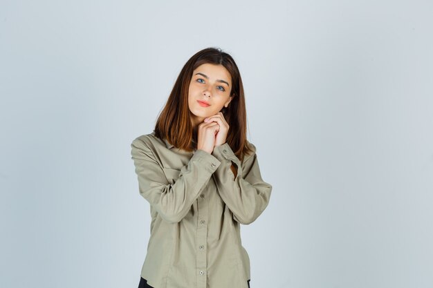 Portrait of young lady propping chin on clasped hands in shirt and looking sensible front view