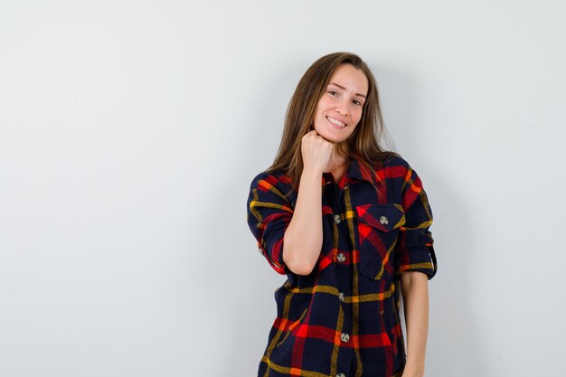 Portrait of young lady propping chin on raised fist in casual shirt and looking delicate front view