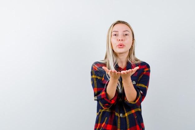 Portrait of young lady sending kiss with hands in checked shirt and looking pretty front view