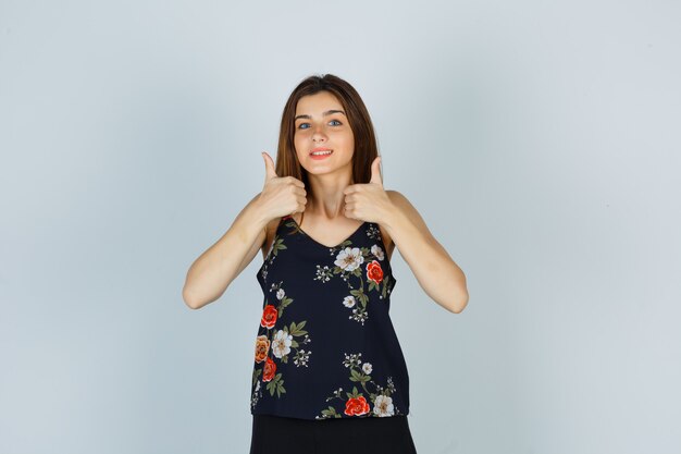 Portrait of young lady showing double thumbs up in blouse and looking cheery front view