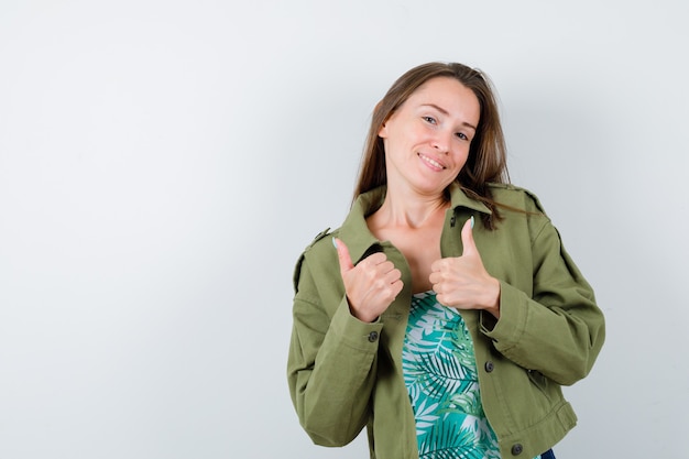 Free photo portrait of young lady showing double thumbs up in green jacket and looking cheery front view
