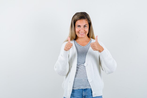 Портрет молодой леди показывает двойные пальцы вверх в футболке, куртке и выглядит счастливым, вид спереди