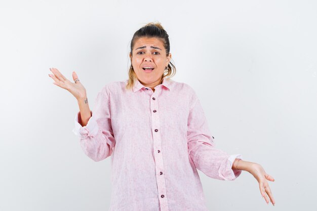 Portrait of young lady showing helpless gesture in pink shirt and looking anxious front view