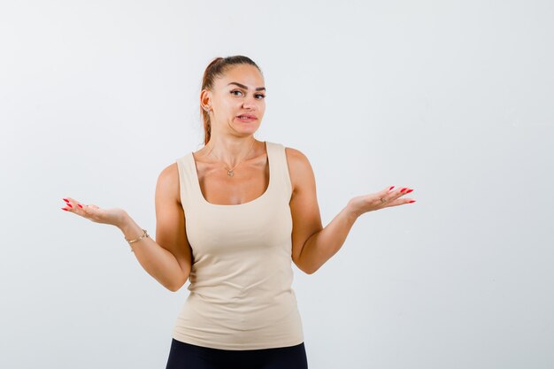 Portrait of young lady showing helpless gesture in tank top and looking confused front view