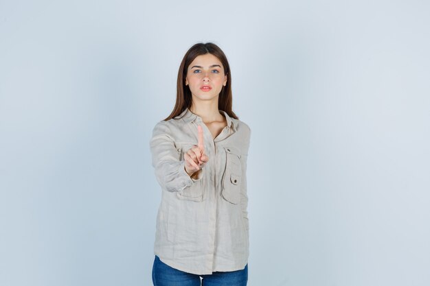 Portrait of young lady showing hold on one minute gesture in casual, jeans and looking confident front view