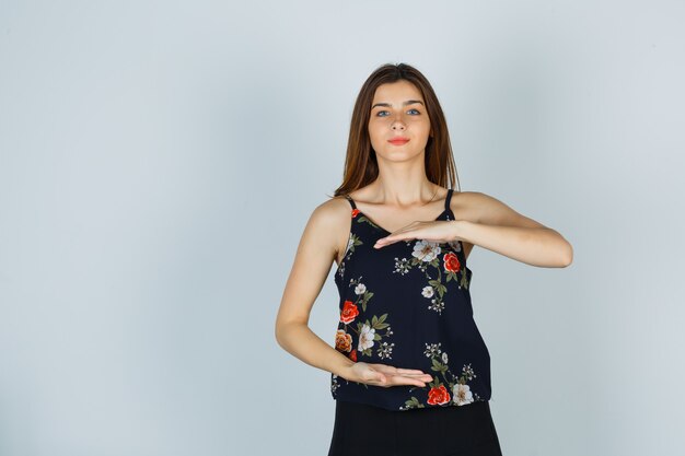 Portrait of young lady showing large size sign in blouse, skirt and looking confident front view