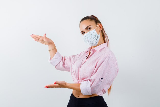 Free photo portrait of young lady showing large size sign in shirt, pants, mask and looking confident front view