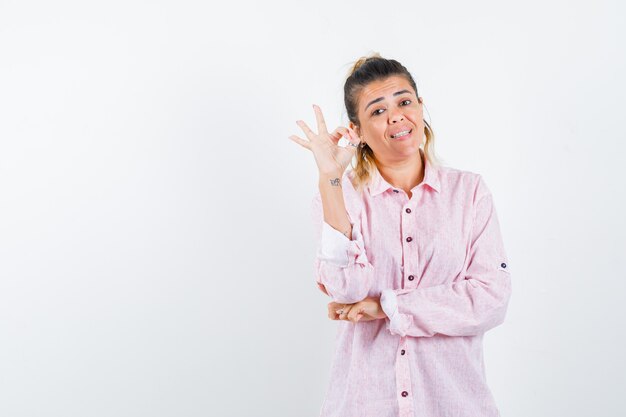 Портрет молодой леди, показывающей жест в розовой рубашке и радостной вид спереди
