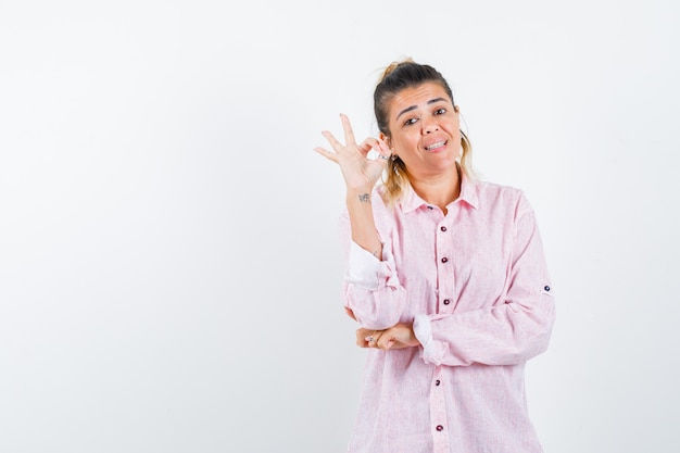 Portrait of young lady showing ok gesture in pink shirt and looking cheery front view