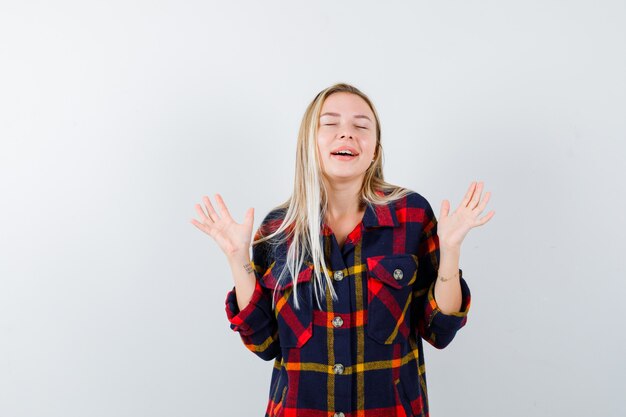 Portrait of young lady showing palms while smiling in checked shirt and looking happy front view