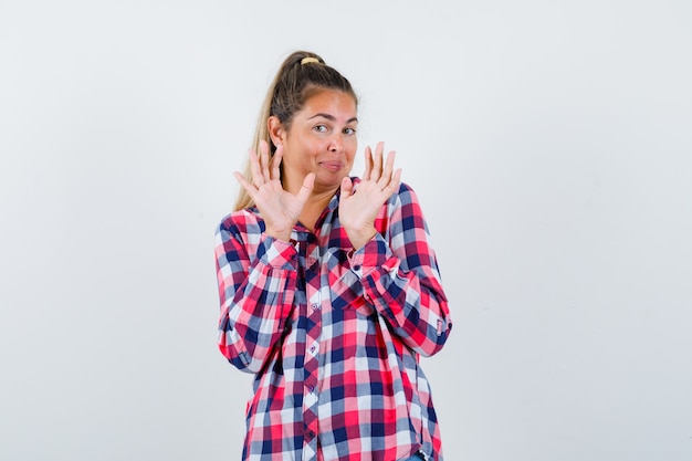 Foto gratuita ritratto di giovane donna che mostra il gesto di rifiuto in camicia controllata e guardando spaventato vista frontale