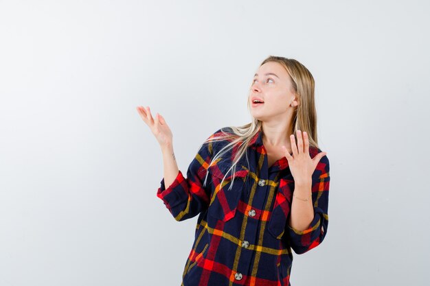 Portrait of young lady showing something in checked shirt and looking amazed front view