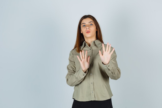 Portrait of young lady showing stop gesture in shirt, skirt and looking scared front view