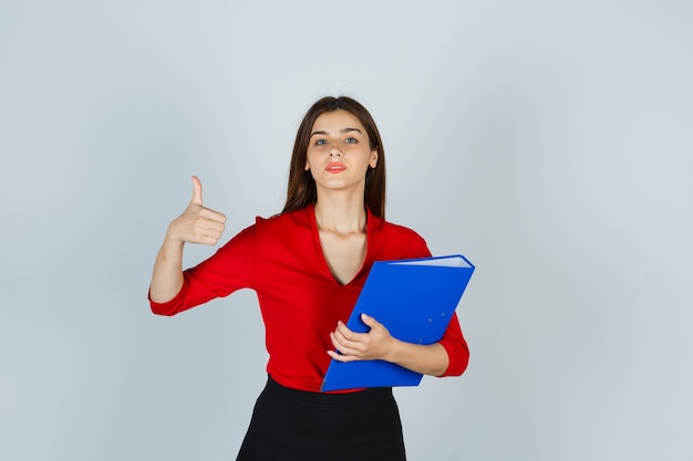 Portrait of young lady showing thumb up while holding folder in red blouse