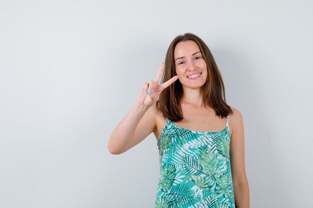 Portrait of young lady showing victory gesture and looking happy front view