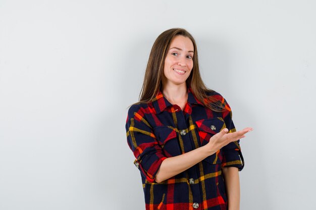 Ritratto di giovane donna che mostra gesto di benvenuto in camicia casual e guardando vista frontale allegra