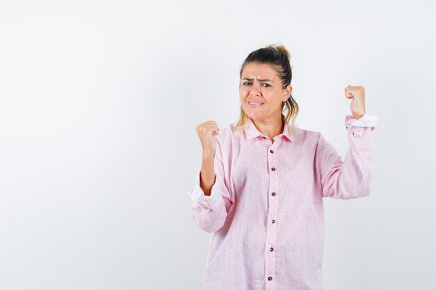 Portrait of young lady showing winner gesture in pink shirt and looking happy front view