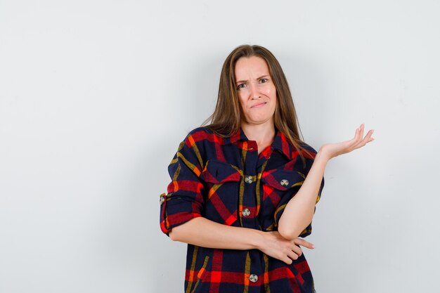 Portrait of young lady spreading palm aside while frowning in casual shirt and looking perplexed front view