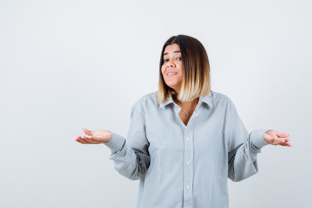 Portrait of young lady spreads palms aside in oversized shir front view