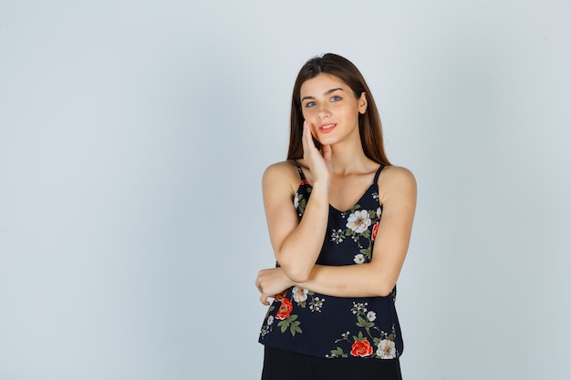 Portrait of young lady touching face skin on her cheek in blouse and looking delicate front view