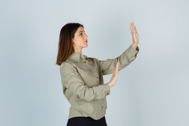 Portrait of young lady trying to block herself with hands in shirt, skirt and looking scared front view