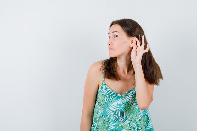 Portrait of young lady with hand behind ear in blouse and looking serious front view