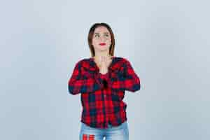 Foto gratuita ritratto di giovane donna con le mani in gesto di preghiera, guardando da parte in camicia a quadri, jeans e guardando grato vista frontale