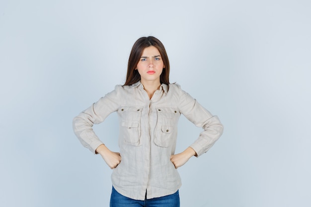 Portrait of young lady with hands on waist in casual, jeans and looking angry front view