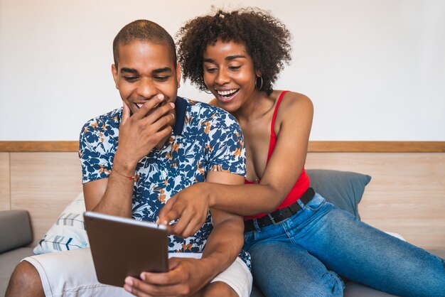 Портрет молодой латинской пары расслабляющий и использующий цифровой планшет дома. Концепция технологии и образа жизни.