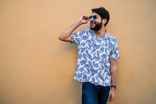 Portrait of young latin man wearing summer clothes and listening to music with earphones against yellow space.