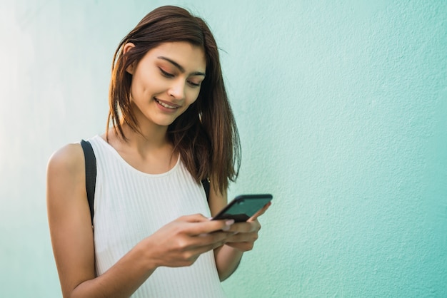 Portrait of young latin woman using her mobile phone outdoors in the street. Urban and communication concept.