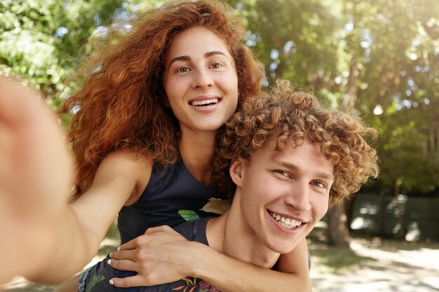 Portrait of young male carrying red-haired woman on his back