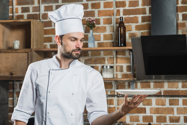 Портрет молодой мужской профессиональный повар, проведение пустой белой тарелке в руке