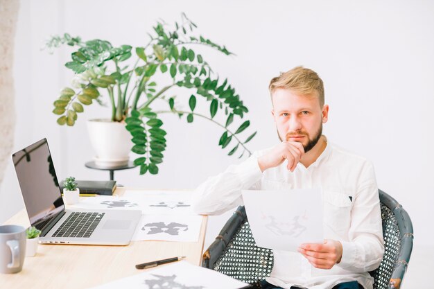 Portrait of a young male psychologist holding rorschach inkblot test paper in hand looking at camera