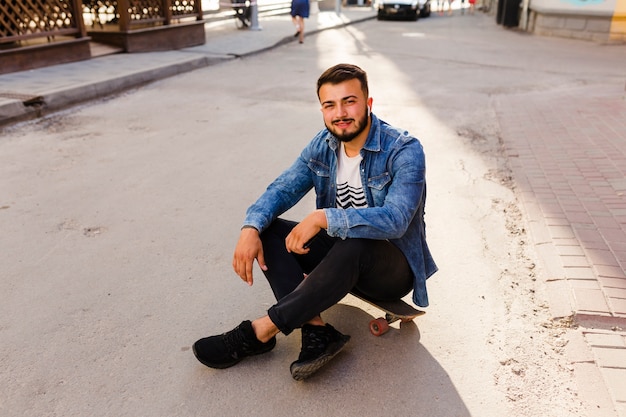 Portrait of a young male skateboarder sitting on skateboard